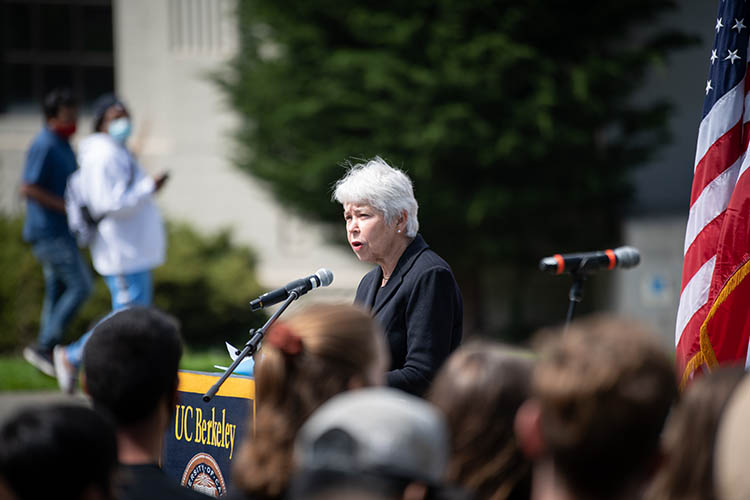 Chancellor Carol Christ, wearing black, talks at a podium