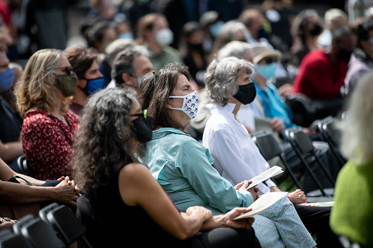 a woman in a Cal mask sits in a crowd during the service
