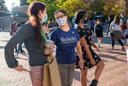 Lisa García Bedolla, in a mask and shirt saying graduate division, talks to a student on sproul plaza