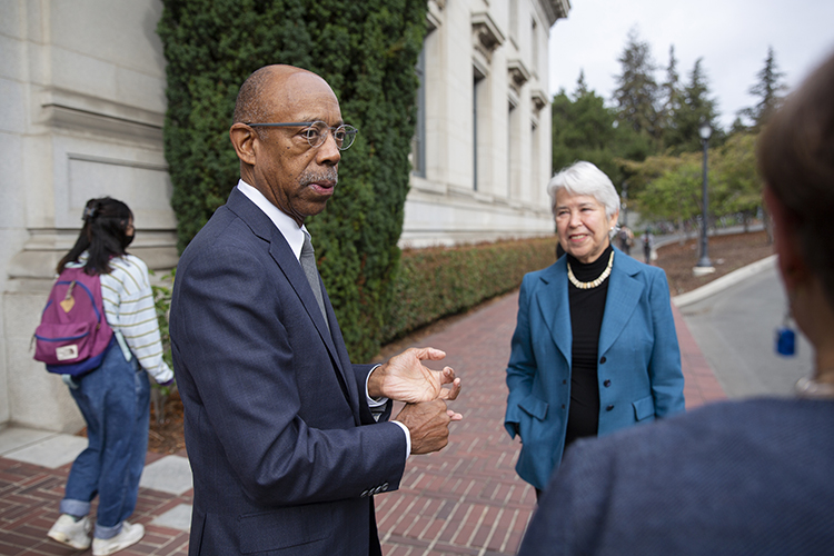 drake, in a suit, talks with chancellor carol christ outside of california hall