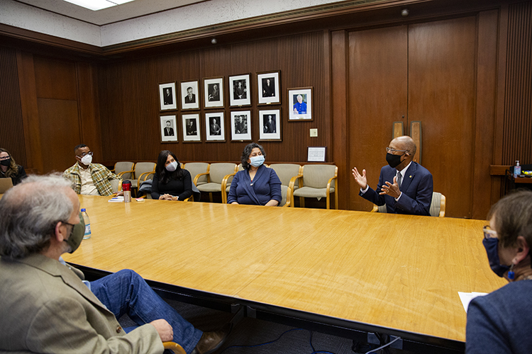 drake talks with people at a big wooden conference table inside california hall