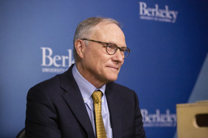 card, in a suit, sits in front of a berkeley branded background