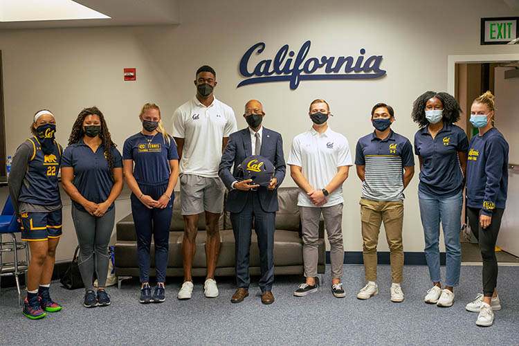 drake stands with student athletes in front of a sign saying california