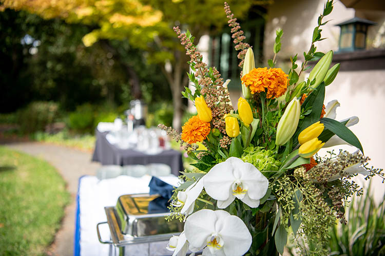 flowers and food on a table with a white tablecloth outside