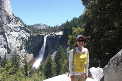 Ann Wai-Yee Kwong on a hike posing next to a lustrous waterfall. on a rocky mountain