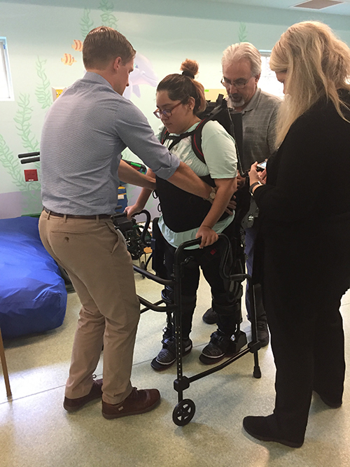 Mariana walks with braces on her legs and a walker during rehab