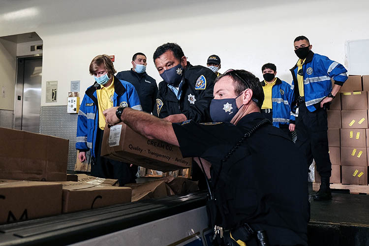 a group of people in masks loads the back of a pick-up truck with boxes