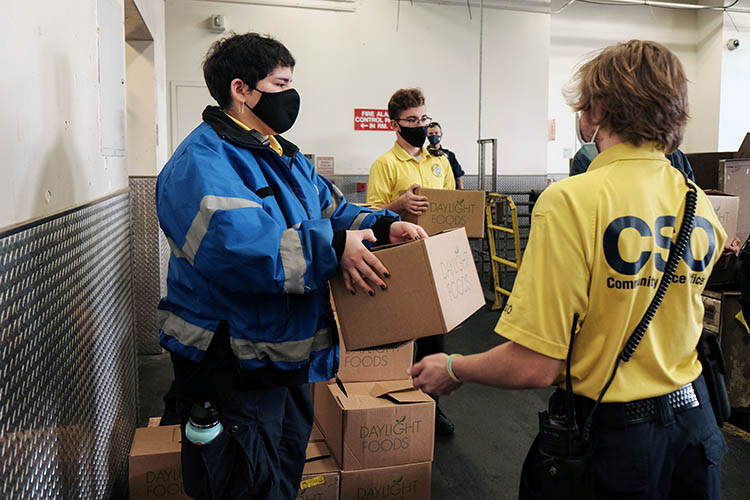 person in blue jacket hands a box to a person in a yellow shirt that says CSO