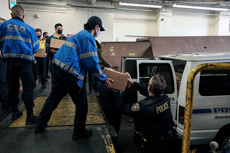 a student in a blue jacket hands frozen turkeys to a police officer standing near a van