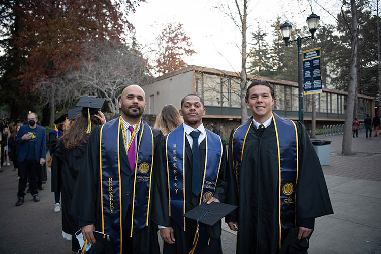 three men stand together outside of the graduation venue