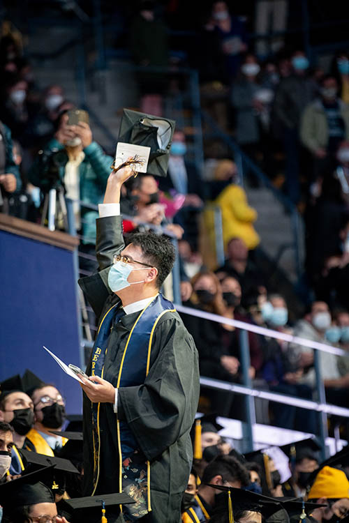 a student in a maks waves his hat in celebration