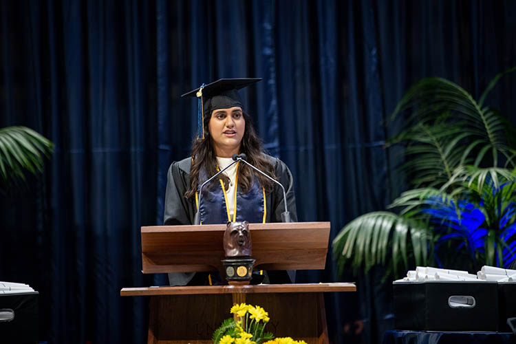 a woman in a cap and gown speaks at a graduation ceremony podium