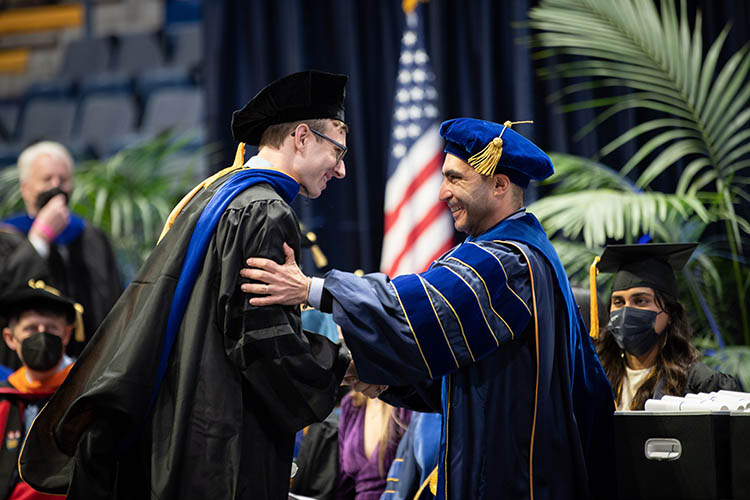 two men in graduation outfits shake hands