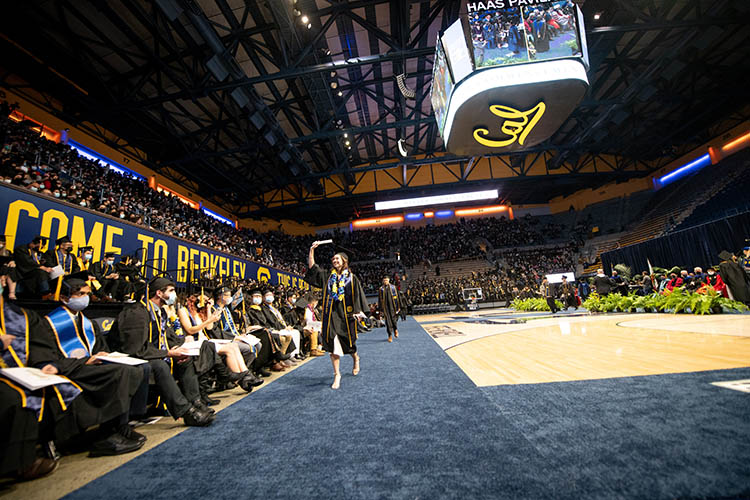 a student waves as he crosses the arena floor. it says 