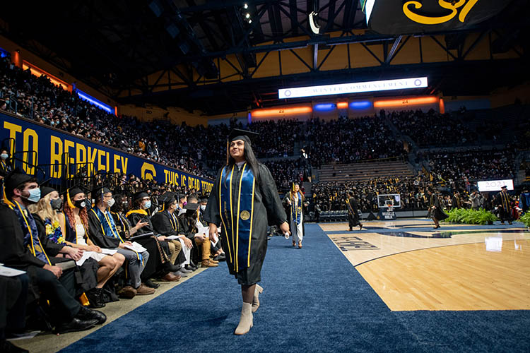 a woman in graduation regalia walks across arena floor