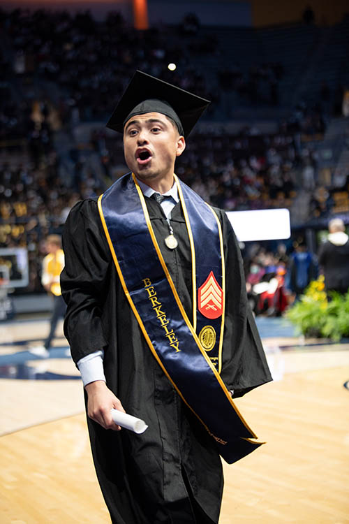 a student in graduation gear cheers as he walks