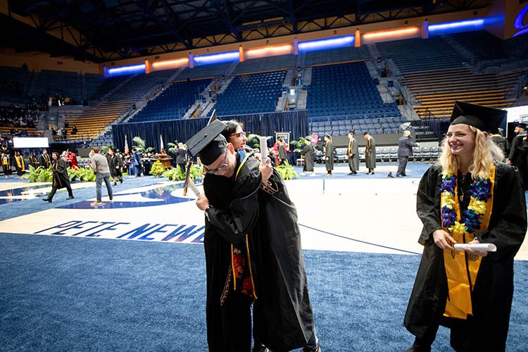 two students in graduation gear hug