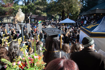 a student in a graduation hat looks out upon a sea of people