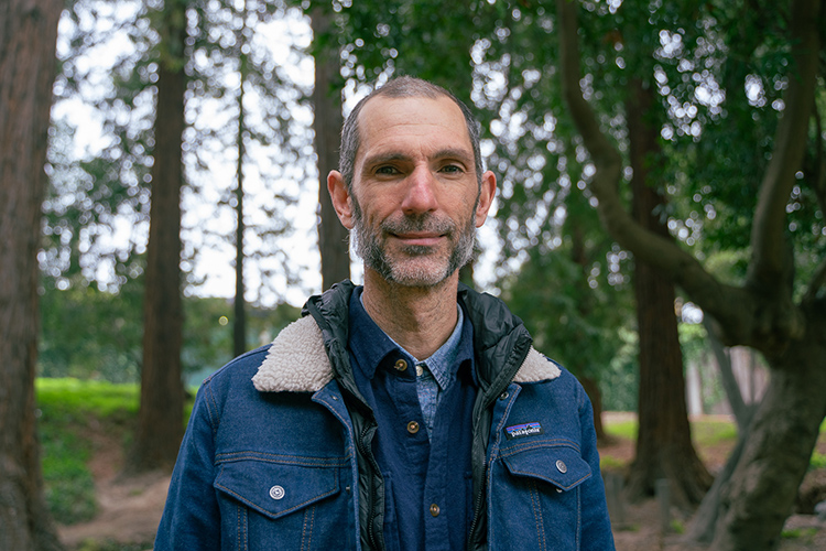 Sean Burns, director of the new UC Berkeley Student Discovery Hun, looks at the camera in a wooded part of campus.