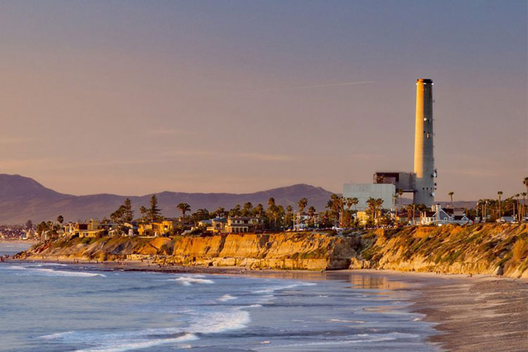 A photo shows a smokestack looming over the California coast at dusk