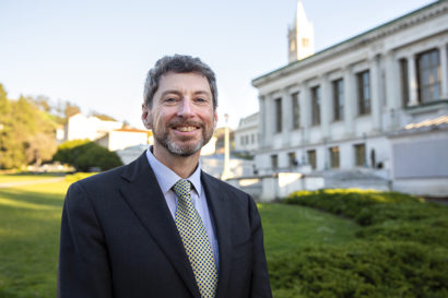 Ben Hermalin, UC Berkeley's newly chosen executive vice chancellor and provost, stands near Memorial Glade with Doe Library and the Campanile in the background and smiles at the camera.