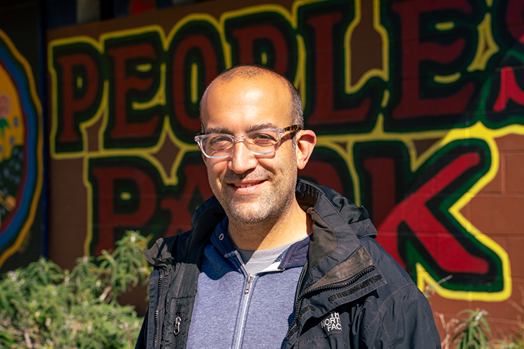 Ari Neulight, a campus social worker who does outreach to the homeless on and near campus, poses next to the words "People's Park" that are painted in colorful letters on a wall in the well-known park near campus.