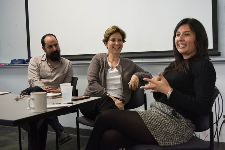 Cristina Mora sitting at a table with two other professors speaking to a group of students.