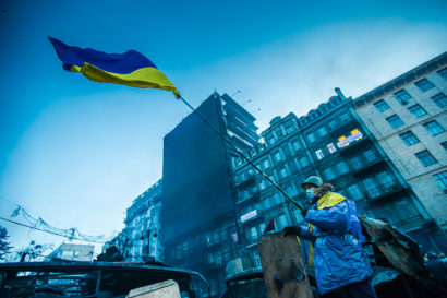 Man raising a Ukrainian flag in front of a dilapidate building