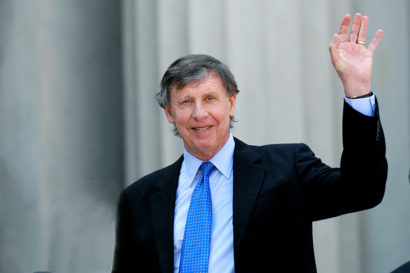 Richard Blum waves at the Greek Theatre wearing a black suit with a blue tie.