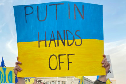 A blue and yellow protest sign that says "Putin hands off."
