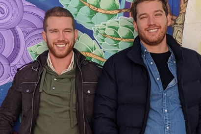 two people standing next to each other smiling in front of a mural