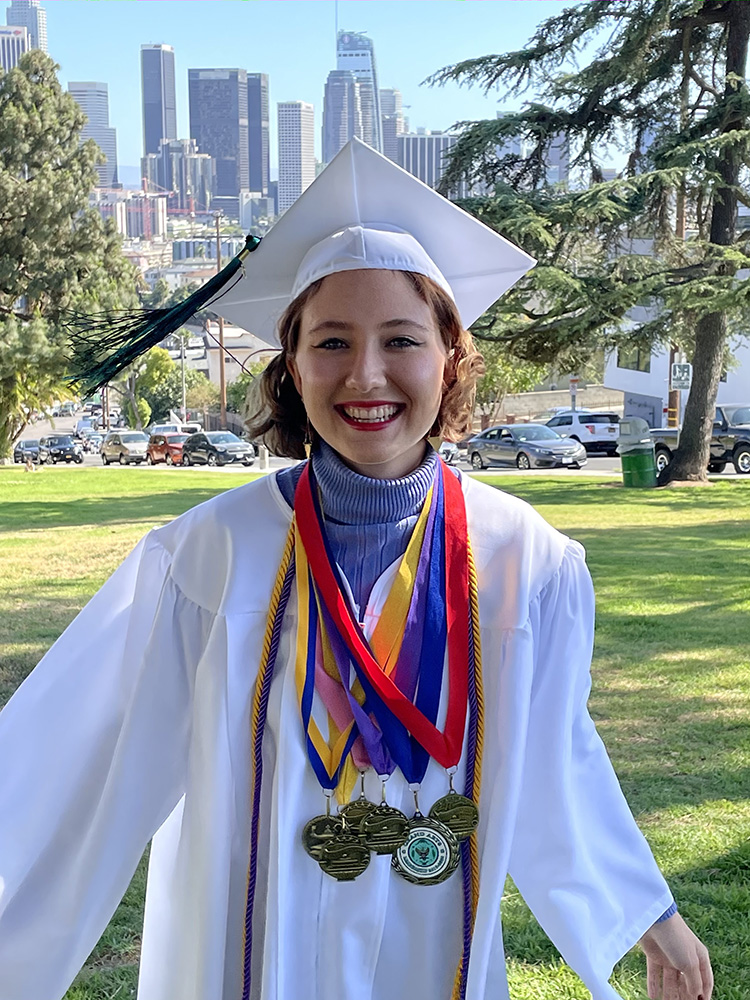 Sofia Liashcheva smiling in her high school graduation gown and wearing medals of achievement.