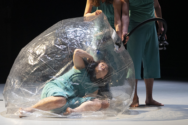 a dancer in a big bubble and two others holding an air supply at a nozzle
