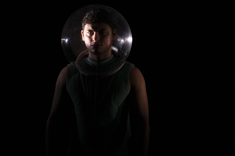 dancer on stage in dark wearing a round bubble thing over their head