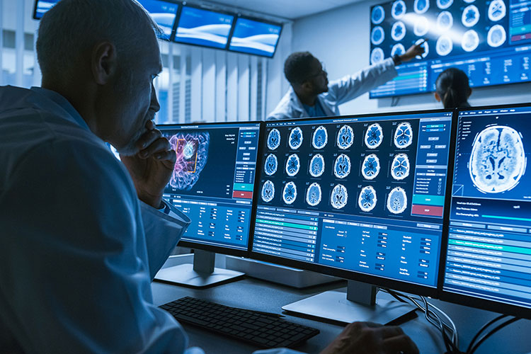 A photo shows a medical professional looking at a computer screen filled with medical scans