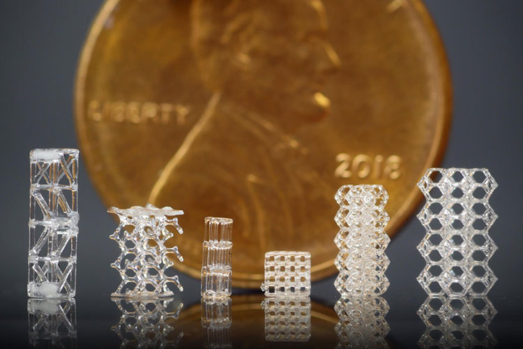 A photo of six small glass lattice structures in different shapes, placed before a penny for scale