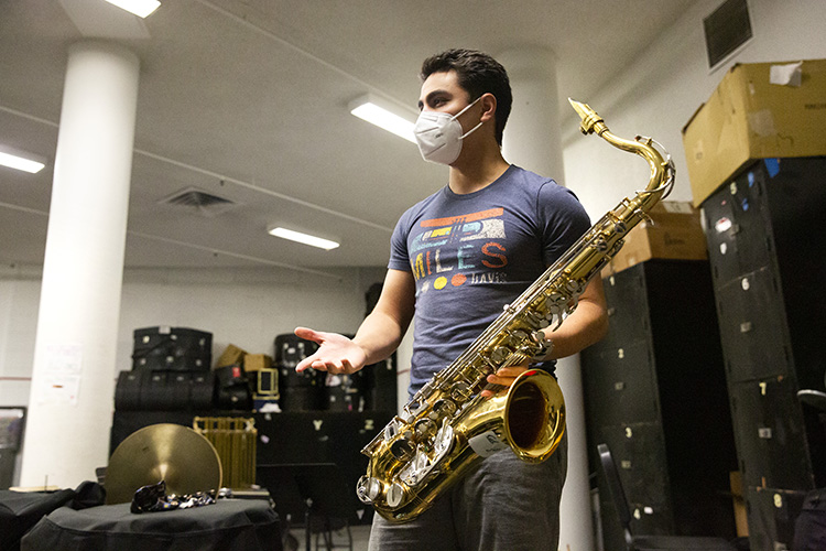 Angela Frisina, a member of the Cal Band, holds his tenor saxophone in the Cal Band practice room. He's wearing a mask during the pandemic.