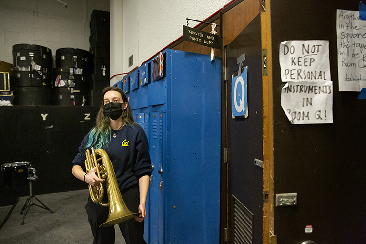 A Cal Band member stands outside of Room Q, a small room off the band's practice room, where she helps repair broken instruments. She's holding a damaged baritone.