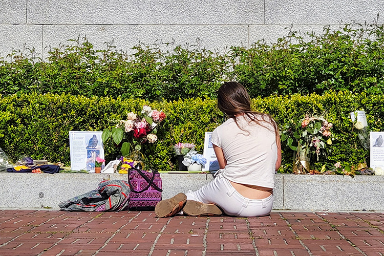 A woman sits on the pavement under the Campanile to look at the tributes left for Grinnell, the Berkeley falcon that was found dead on March 31, 2022.