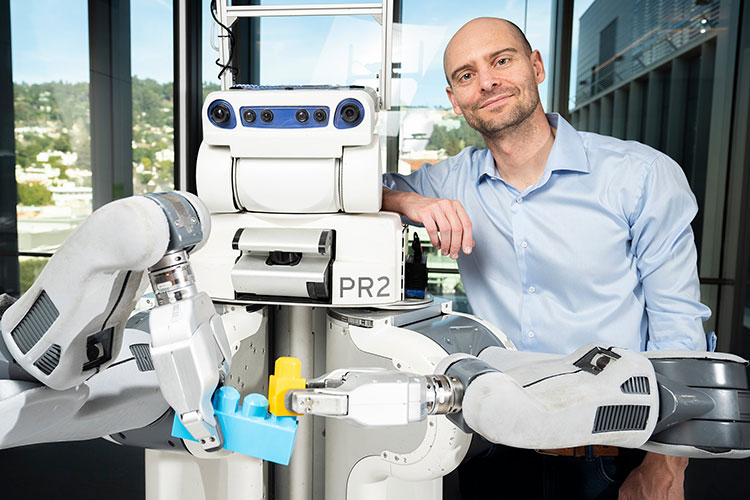 A photo of Pieter Abbeel standing next to a robot