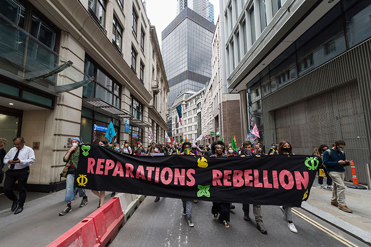 A photo shows protestors marching down a city street holding a large sign that reads 