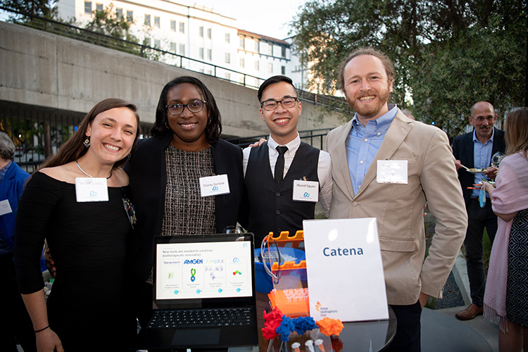 A group of people smiling with a laptop outside.