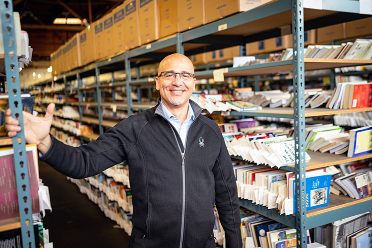 William Rogers stands in front of shelves of books