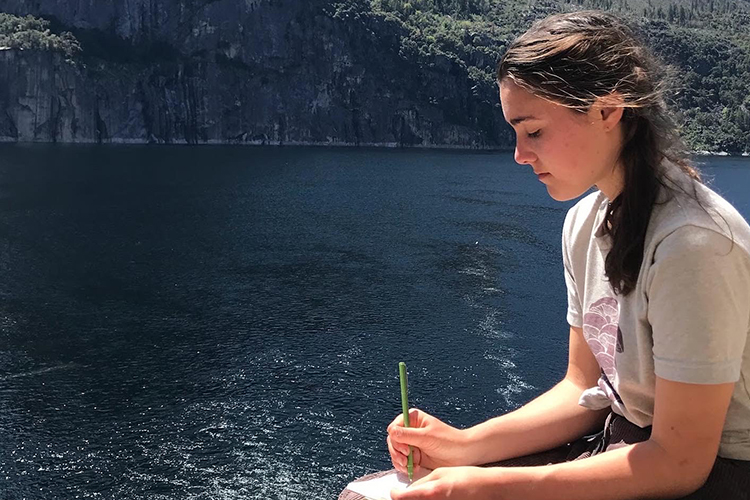 Cora Conner, a student at Sierra College in the Sierra, works on a drawing by sitting beside a beautiful lake.
