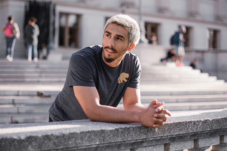 Jonny Hale, a Berkeley student with bleached hair and wearing a T-shirt leans on a concrete railing and looks to the left.