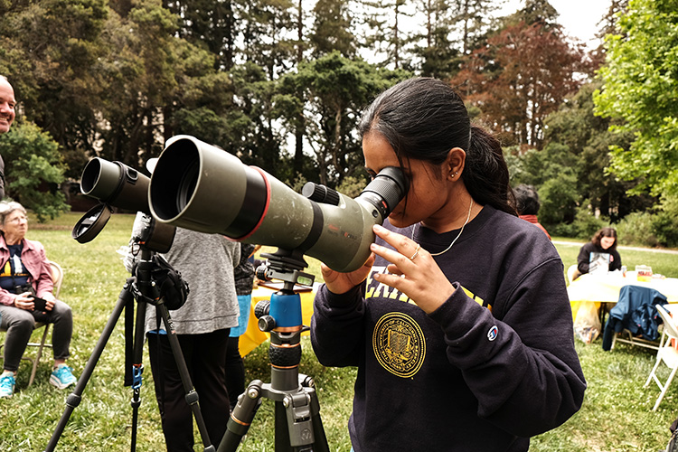 A student peers through a telescope at the Hatch Day festivites on campus to see if she can spot a falcon around or on the Campanile.