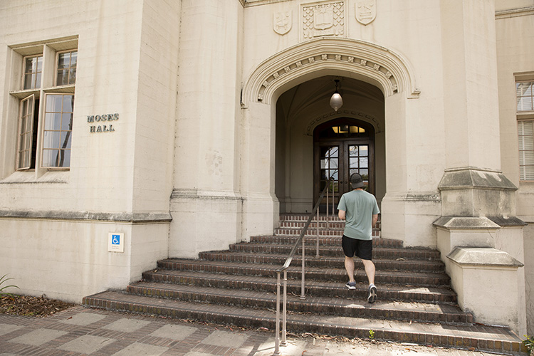 A man walks into Moses Hall, climbing the steps wearing athletic shoes, shorts, a T-shirt and a cap.