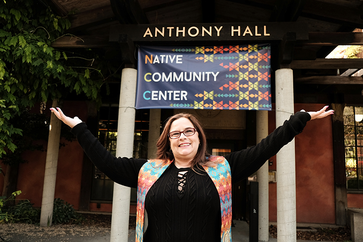 a person stands and smiles under a sign that reads "Native Community Center"