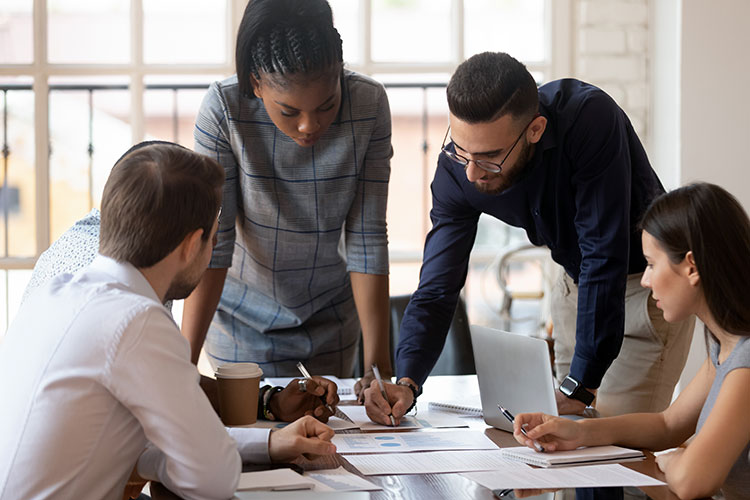 a team of four diverse people, two standing, two sitting, working intently on a project