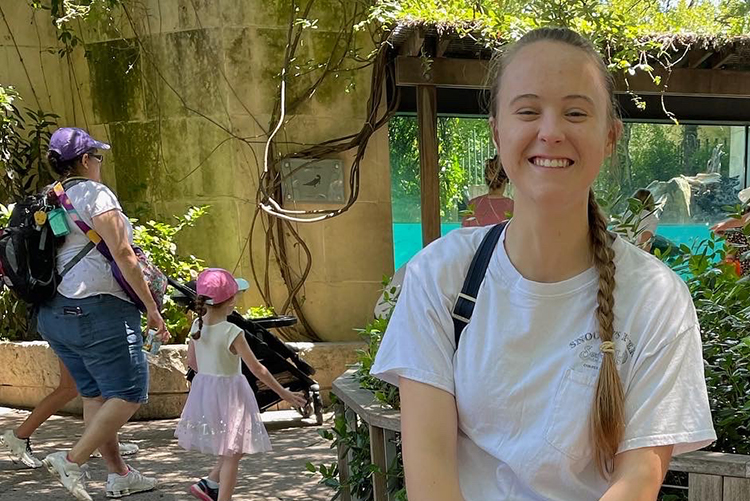 A photo of Grace Millsap shows her sitting on a sculpture of a tortoise at what looks like a zoo. She's smiling and has her eyes nearly closed.